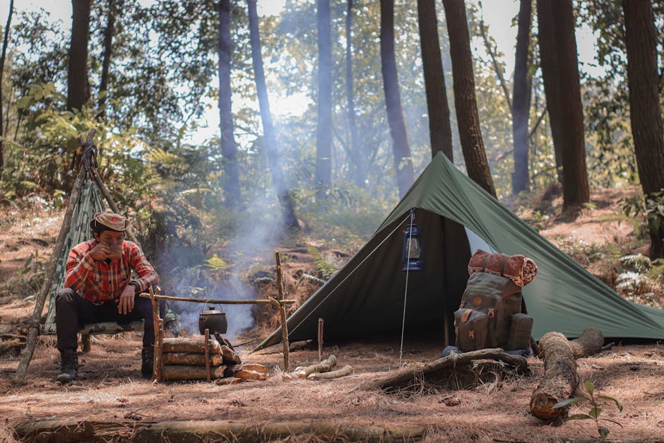 Man camping in forest, sitting by campfire with tent and backpack.